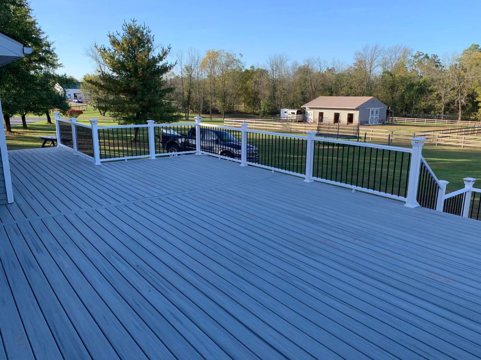 Wide open composite deck with a contrasting board running across it and white railings with black balusters overlooking a farm property