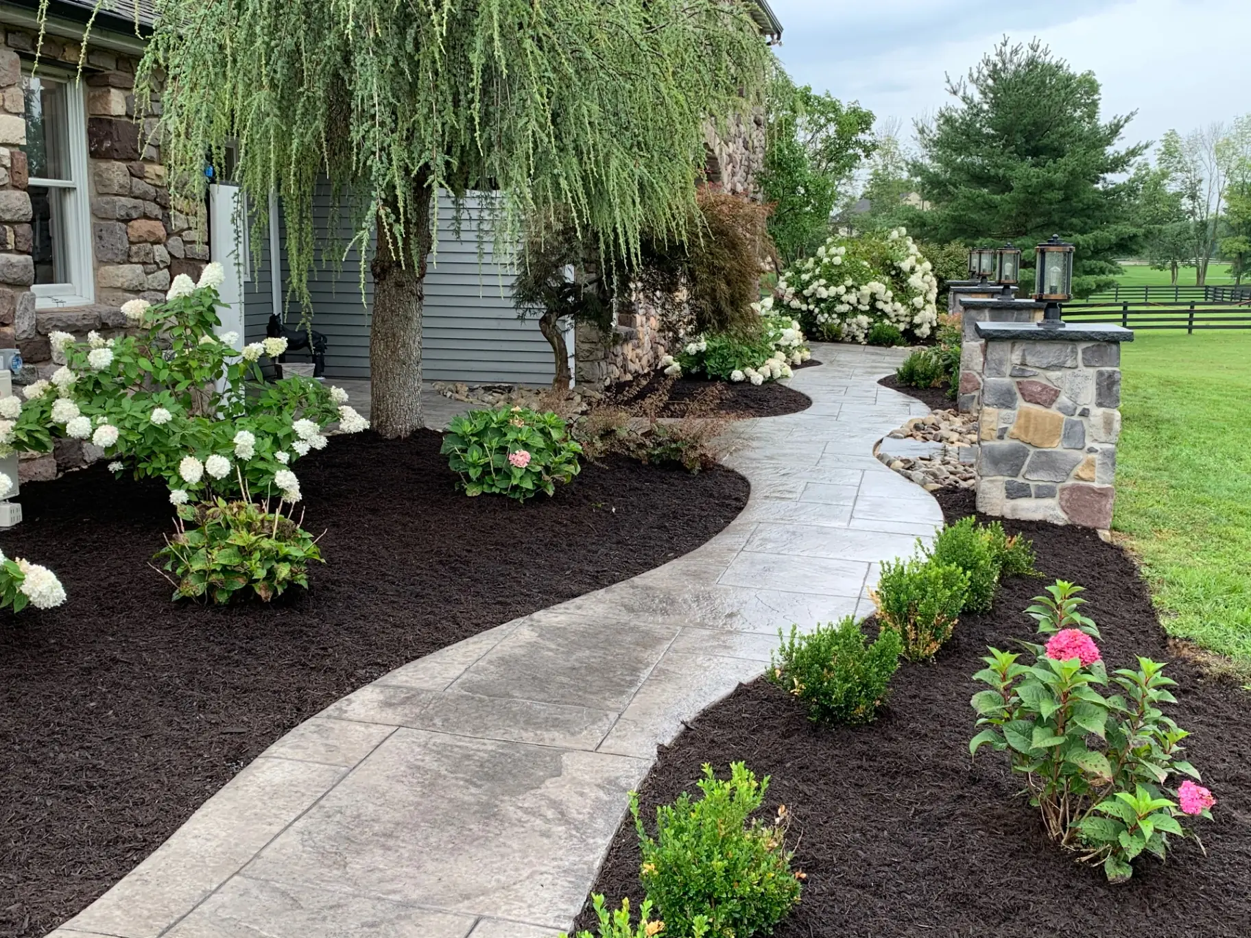 Curved stamped concrete walkway lined with new planting beds and Eldorado Stone pillars with lanterns in Buckingham, PA