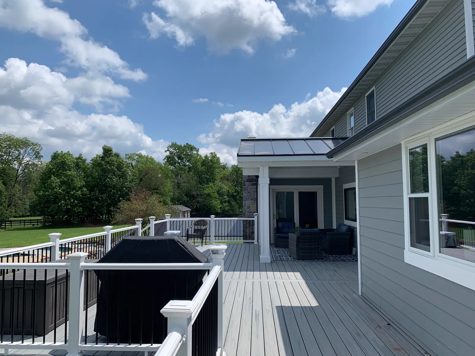 Long view along the deck toward the covered sitting area, with white railings and black balusters and a wide lawn beyond