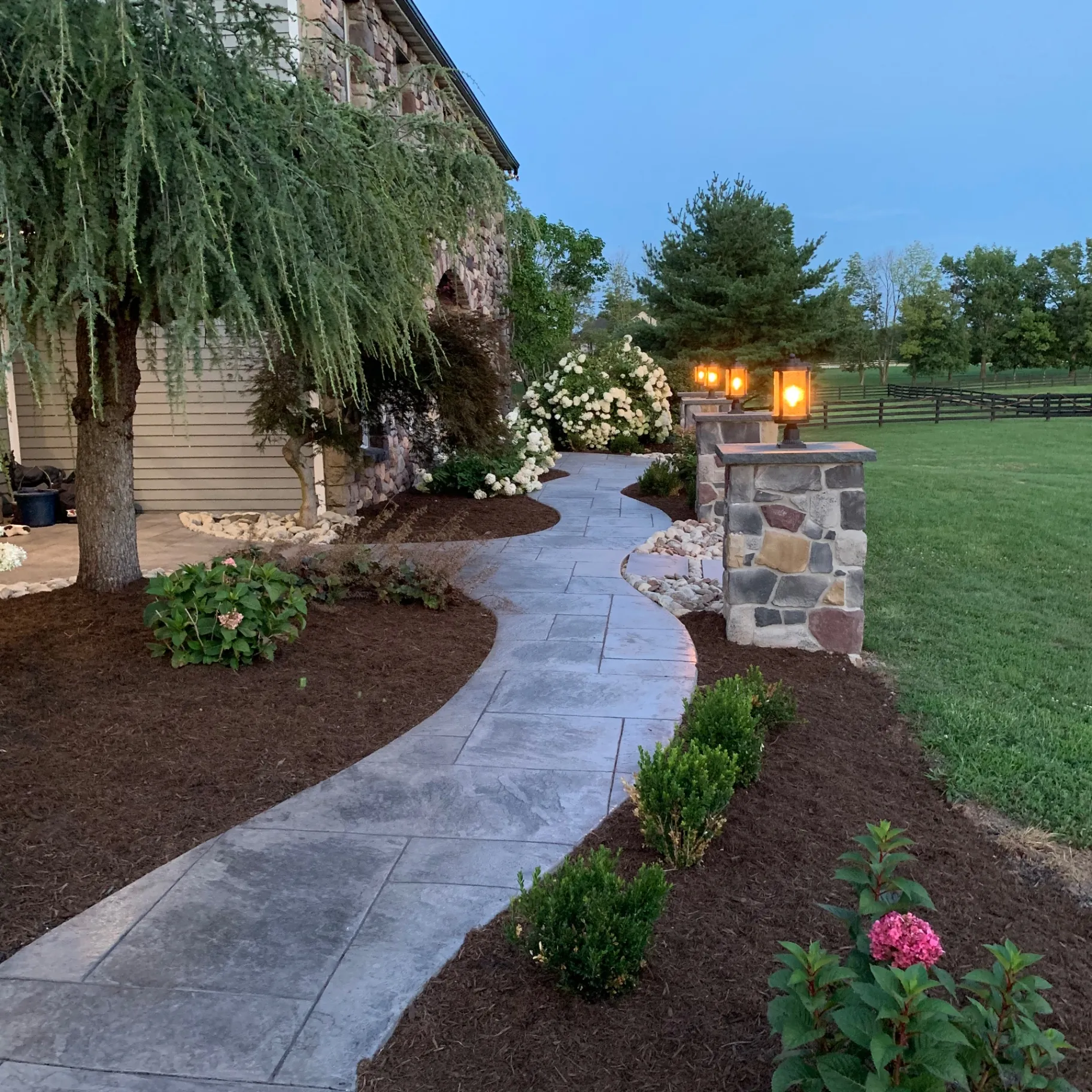 Lit lanterns on Eldorado Stone pillars along a stamped concrete walkway in the evening, Buckingham, PA