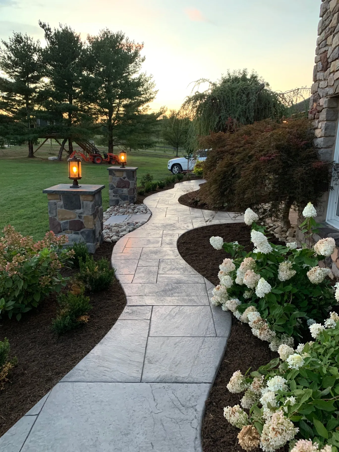 Stamped concrete walkway with a stone-slab texture curving between planting beds at dusk, Buckingham, PA